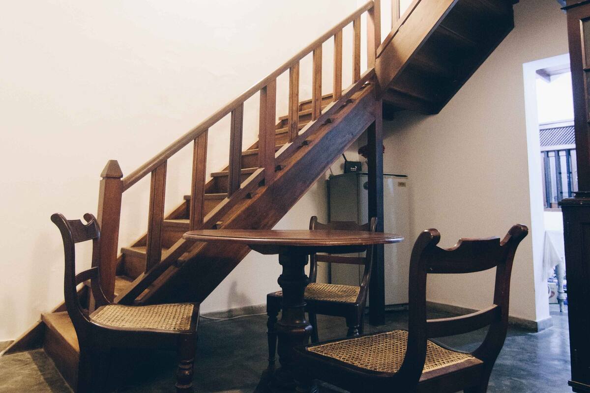 A staircase with wooden railings and chairs in a room with a concrete floor and white walls.