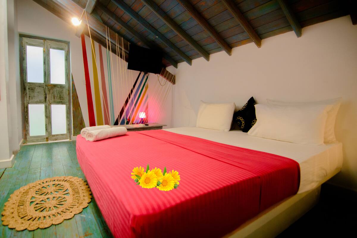 A bedroom with a red bedspread, white pillows, and a wooden floor.