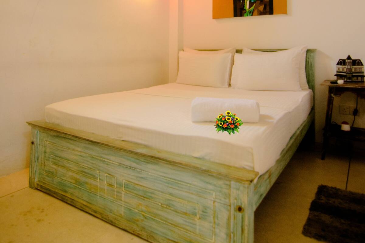 A bedroom with a wooden bed, a ceiling fan, a painting on the wall, and a window with curtains.