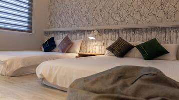 A bedroom with two beds, a patterned wallpaper, a nightstand with a lamp, and a window with blinds.