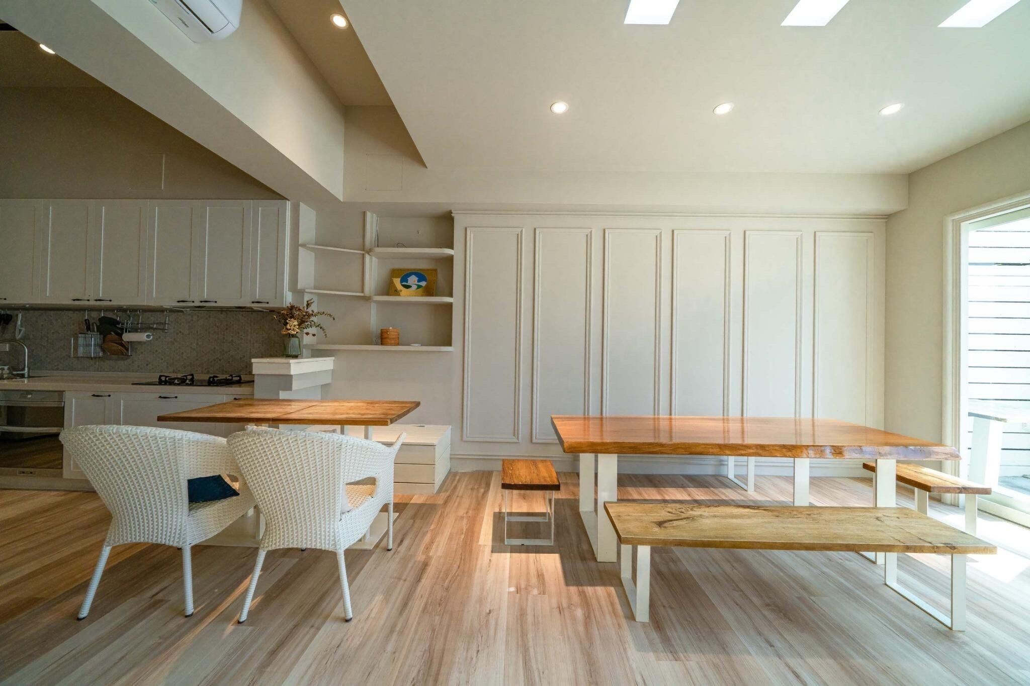 A modern kitchen with white cabinetry, a wooden dining table, and two white wicker chairs.