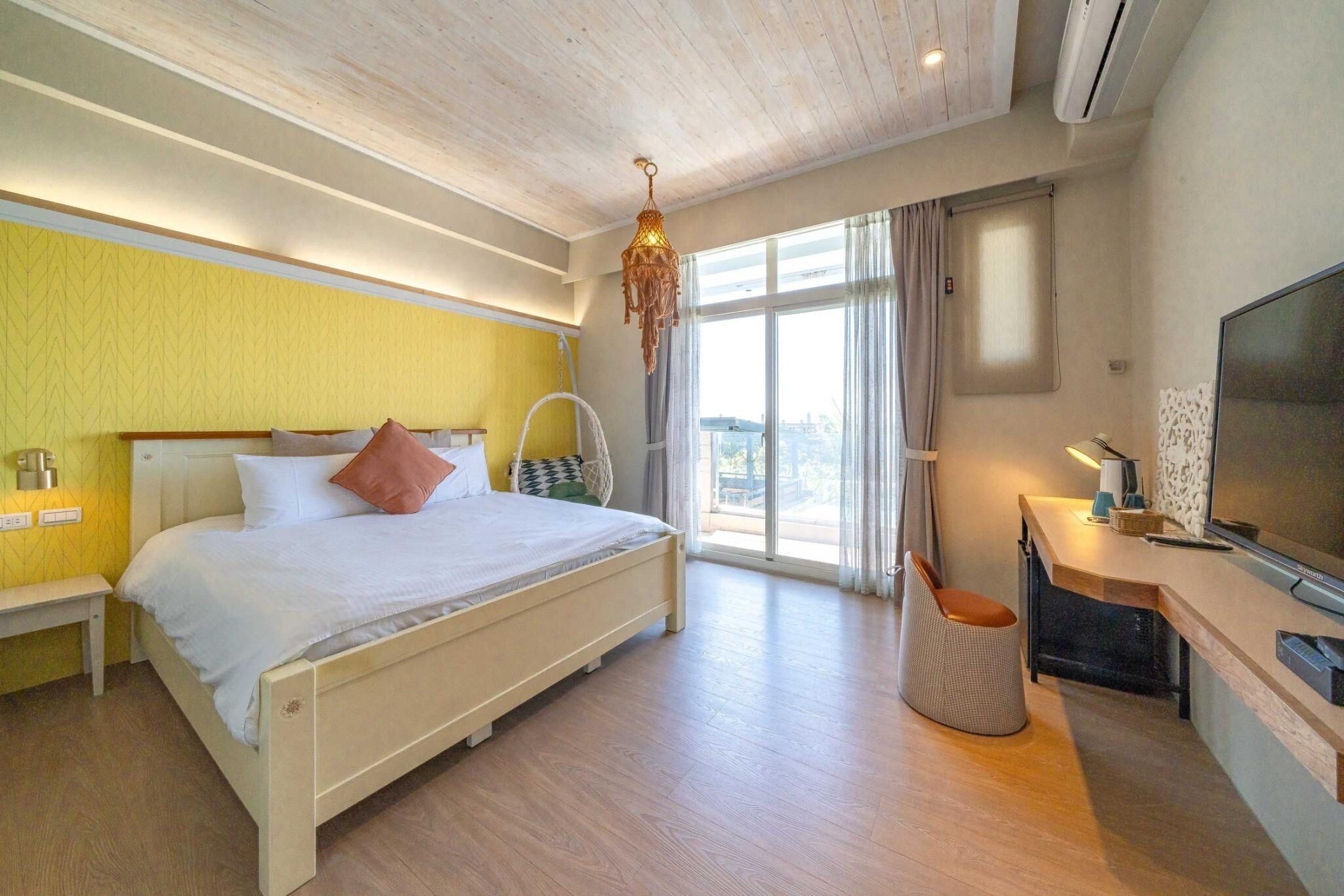 A modern hotel room with a large bed, a desk with a flat-screen TV, and a large window with curtains.
