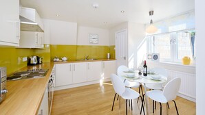 A modern kitchen with white cabinets, a yellow backsplash, and a dining area with white chairs and a table. - Home from Home Aberdeen (Aberdeen)