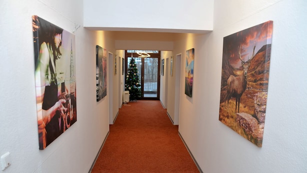 A hallway with a red carpet, flanked by framed artwork on the walls, leading to a door with a Christmas tree and a modern light fixture. - Gästehaus beim Prinz (Kuerten)