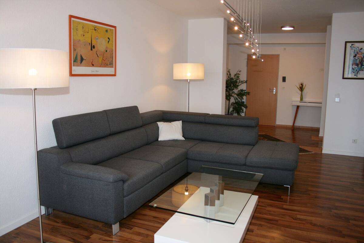 A modern living room with a grey sectional sofa, a glass coffee table, and two floor lamps.