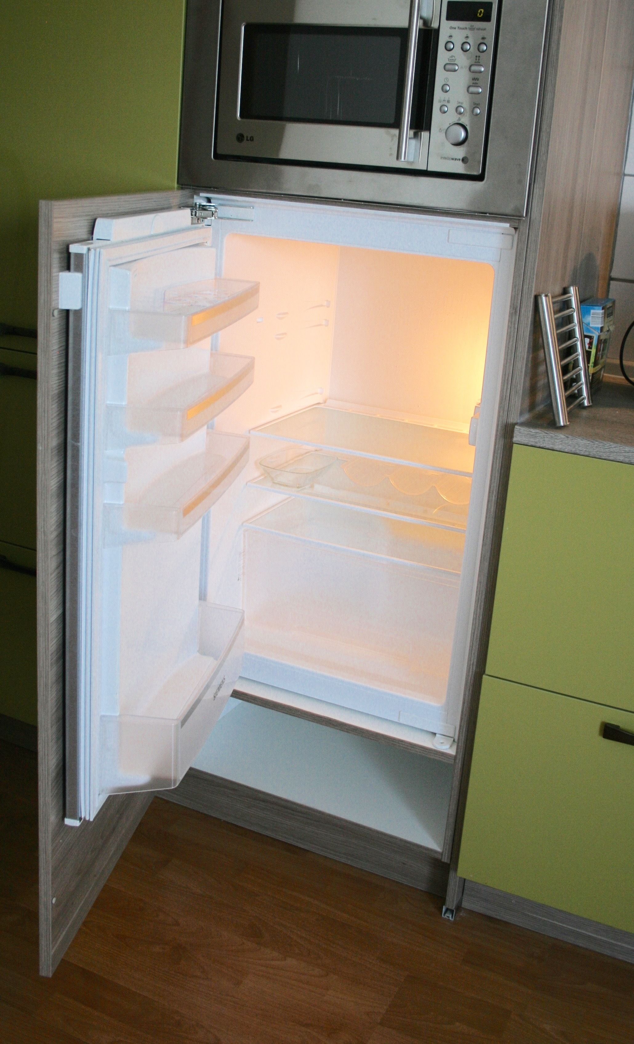 An open refrigerator with multiple shelves and a microwave above it.