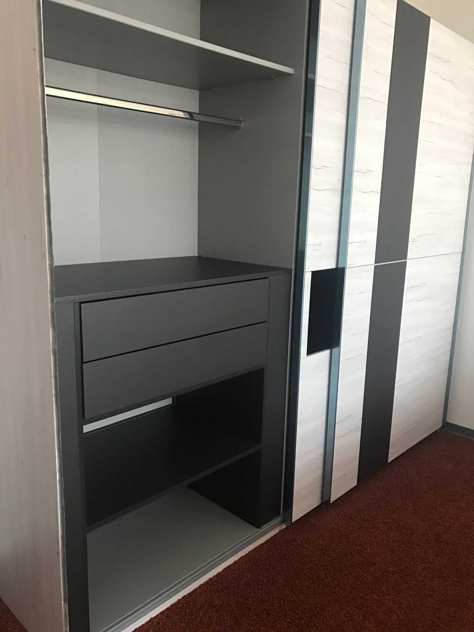 A modern, minimalist room with a grey wardrobe, a small desk, and a shelving unit.