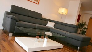 A modern living room with a grey sofa, a glass coffee table, and a floor lamp. - Gästehaus beim Prinz (Kuerten)