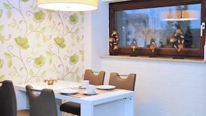 A dining area with a white table, brown chairs, and a window with decorative lamps. - Gästehaus beim Prinz (Kuerten)