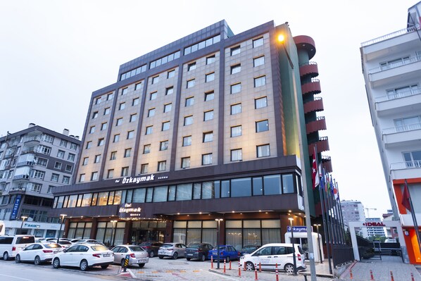 Ein mehrstöckiges Hotel mit moderner Fassade, einem Restaurant im Erdgeschoss und einem Parkplatz mit mehreren Autos.