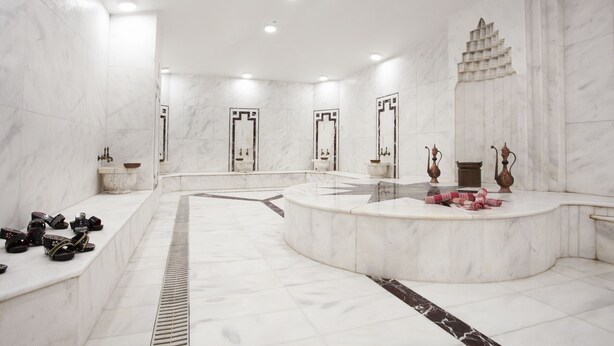 Une salle de bain spacieuse avec un meuble-lavabo incurvé, des murs en marbre et plusieurs vasques.