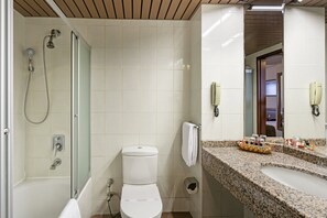 Ein Badezimmer mit einer gläsernen Duschkabine, einer Toilette, einem Waschbecken mit Granitplatte und zwei an der Wand befestigten Telefonen.