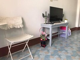 A small room with a white chair, a desk with a TV, a candelabra, and a vase with flowers.
