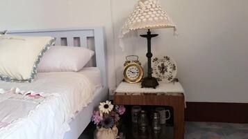 A bedroom with a bed, a bedside table with a lamp, a clock, and a small cabinet with mugs.