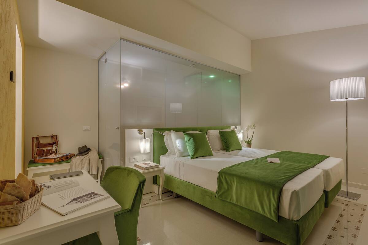 A hotel room with a large bed, a desk with a chair, a small table, and a lamp.