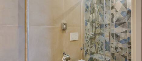 A bathroom with a glass shower enclosure, a toilet, and a sink.