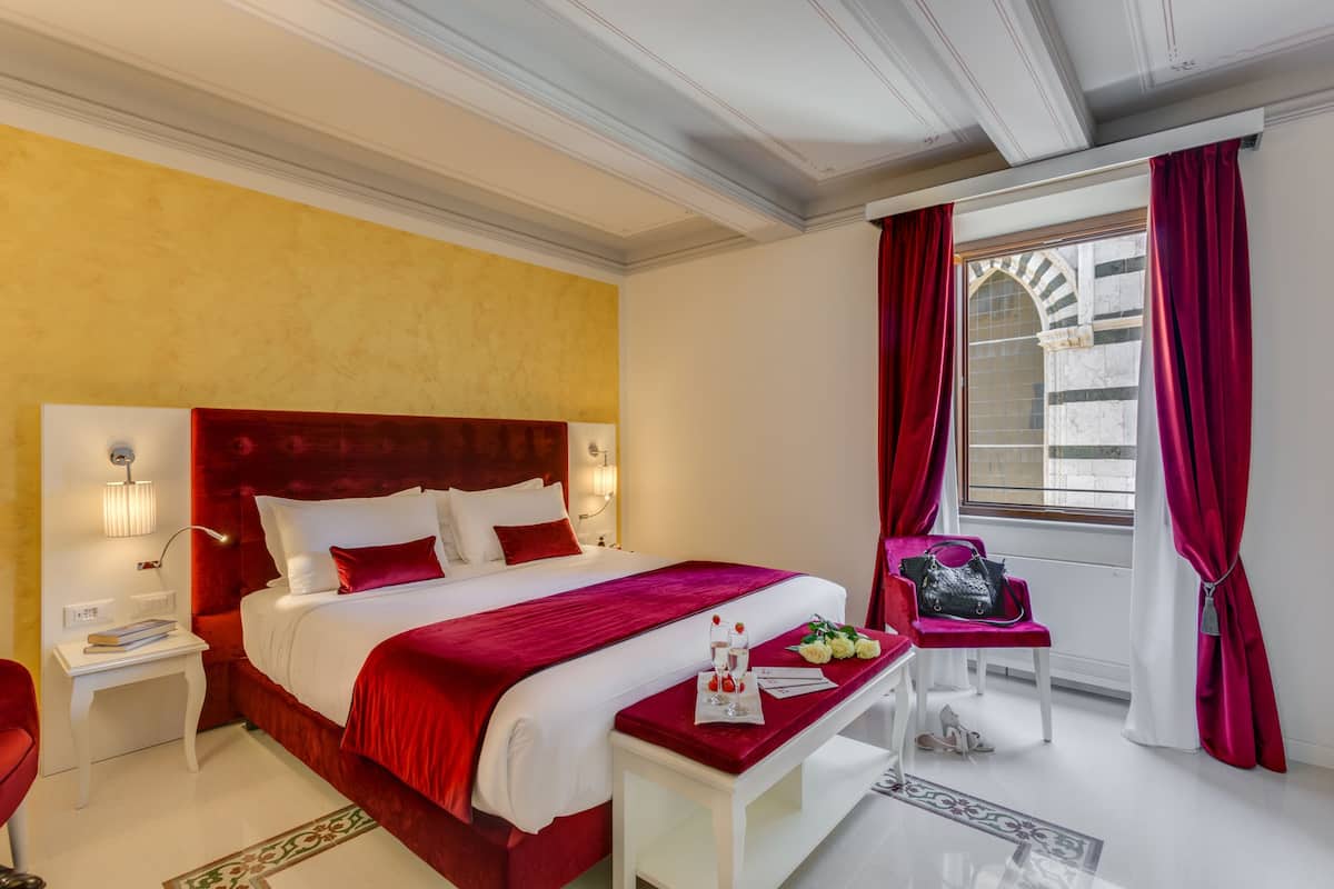 A hotel room with a large bed, a nightstand, a desk, a chair, and a window with curtains.
