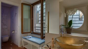 A bathroom with a marble vanity, a large gold sink, a window with a view, and a potted orchid.