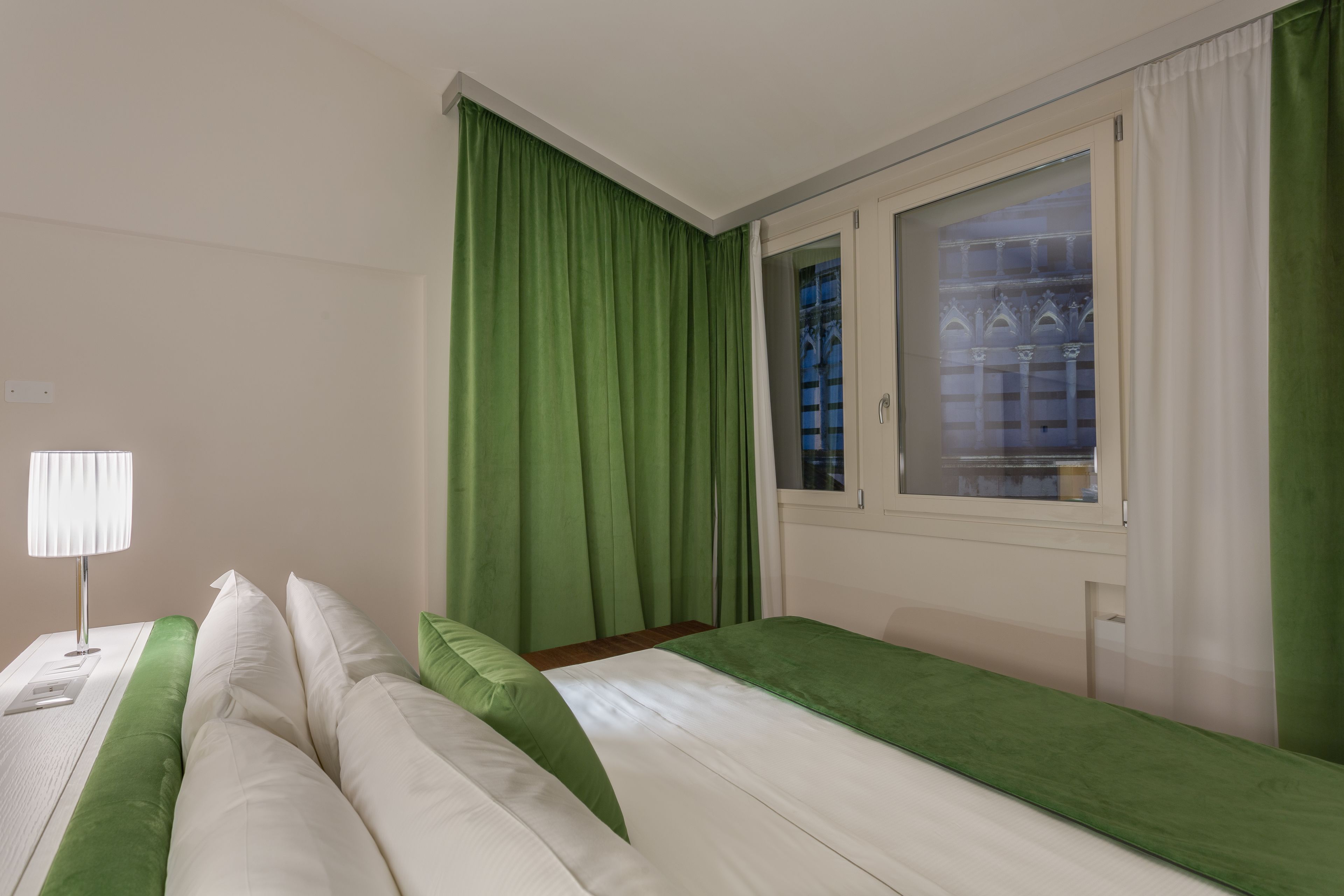 A hotel room with a bed, a nightstand, a lamp, and a window with curtains.