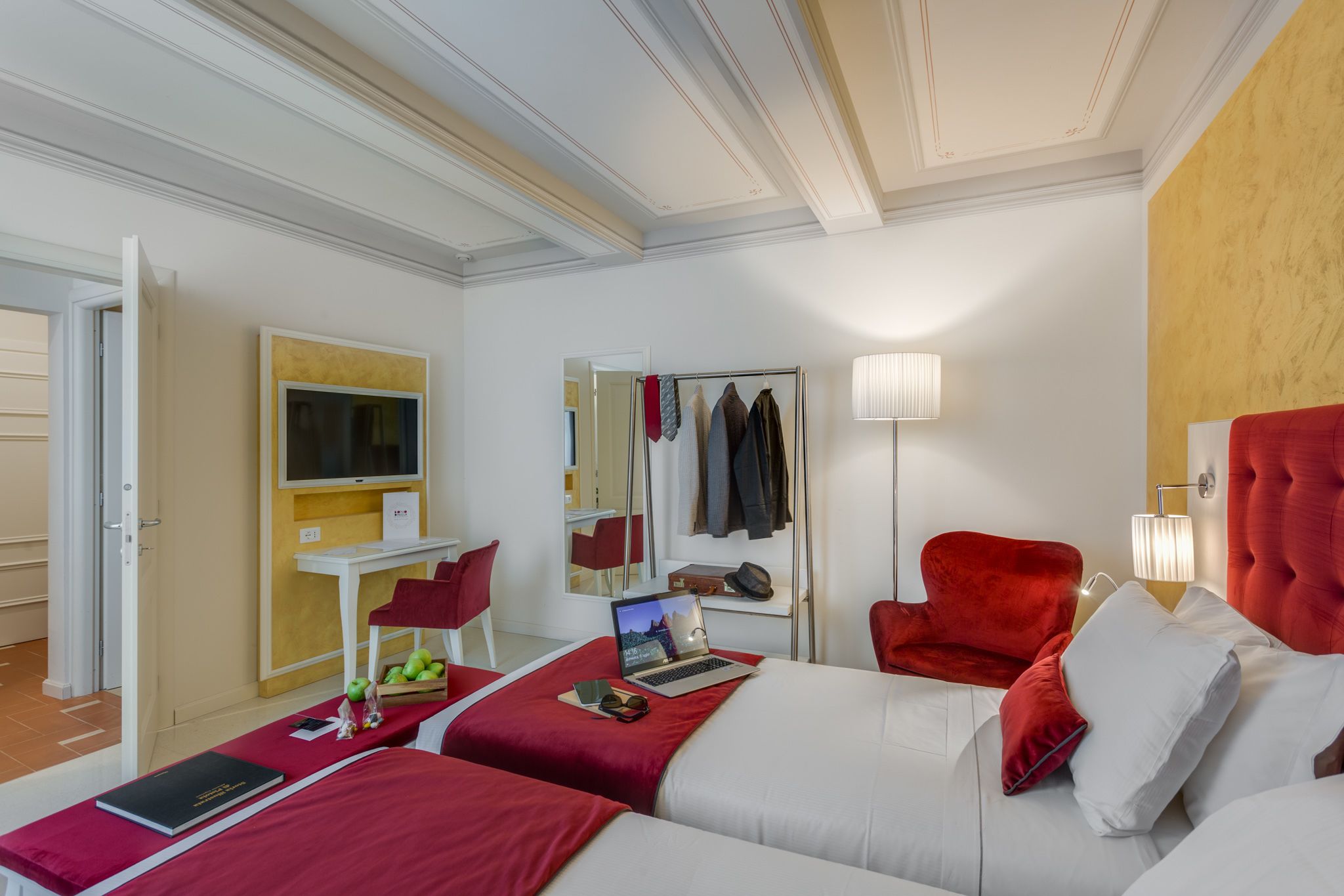 Une chambre d’hôtel avec deux lits, un bureau avec un ordinateur portable, un miroir, une chaise rouge et un téléviseur.