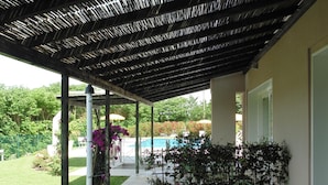 A covered patio area with a pool, green chairs, and potted plants. - Agriturismo Dell'orto (Verona)