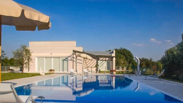 A modern pool area with a clear blue pool, lounge chairs, and a covered seating area. - Agriturismo Dell'orto (Verona)