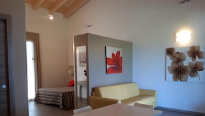 A modern, well-lit room with a dining table, a sofa, and a bed. There are floral paintings on the walls and a door with a handle. - Agriturismo Dell'orto (Verona)