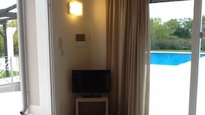 A room with a television on a stand, a sliding glass door leading to an outdoor area, and a small light fixture on the wall. - Agriturismo Dell'orto (Verona)