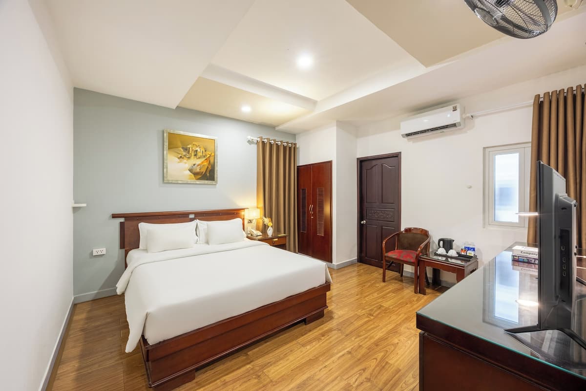 Ein Hotelzimmer mit einem großen Bett, einem Schreibtisch mit Fernseher, einer Klimaanlage und einem Bild an der Wand.