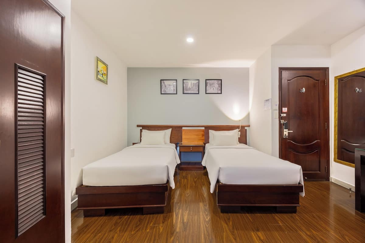 Ein Hotelzimmer mit zwei Betten, Holzboden, einem Holz-Kopfteil, einem kleinen Nachttisch und einer Tür mit goldener Rahmung.