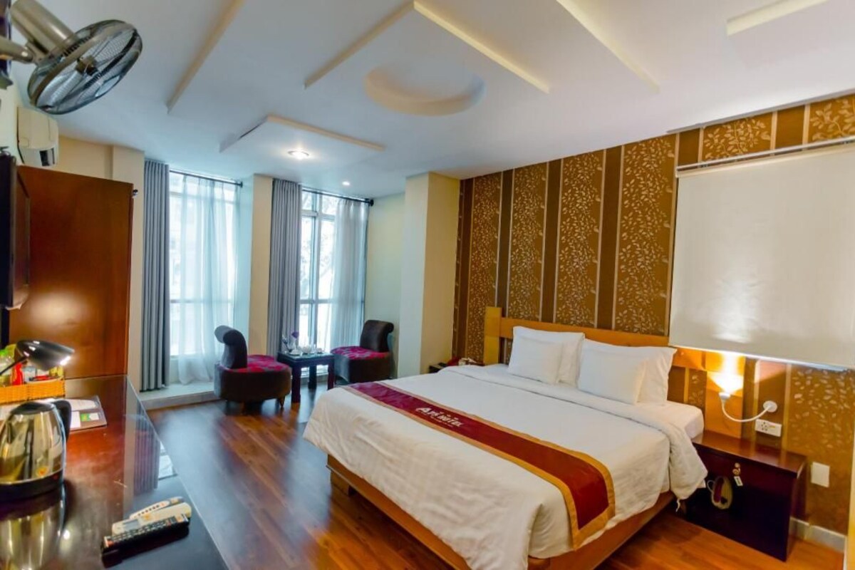 Une chambre d’hôtel avec un grand lit, un bureau avec une lampe, une chaise, une télévision et une fenêtre avec des rideaux.