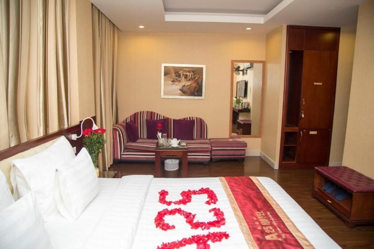 Une chambre d’hôtel avec un lit, un canapé, une petite table sur laquelle est posé un vase de fleurs et une armoire en bois.