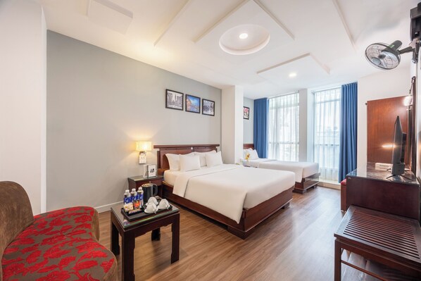 Habitación de hotel con una cama grande, una cama más pequeña, un escritorio con una lámpara, una silla y un sofá.