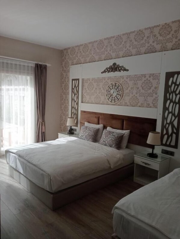 A hotel room with a large bed, a bedside table with a lamp, a decorative wall clock, and a window with curtains. - Alacati The Design Hotel (Cesme)