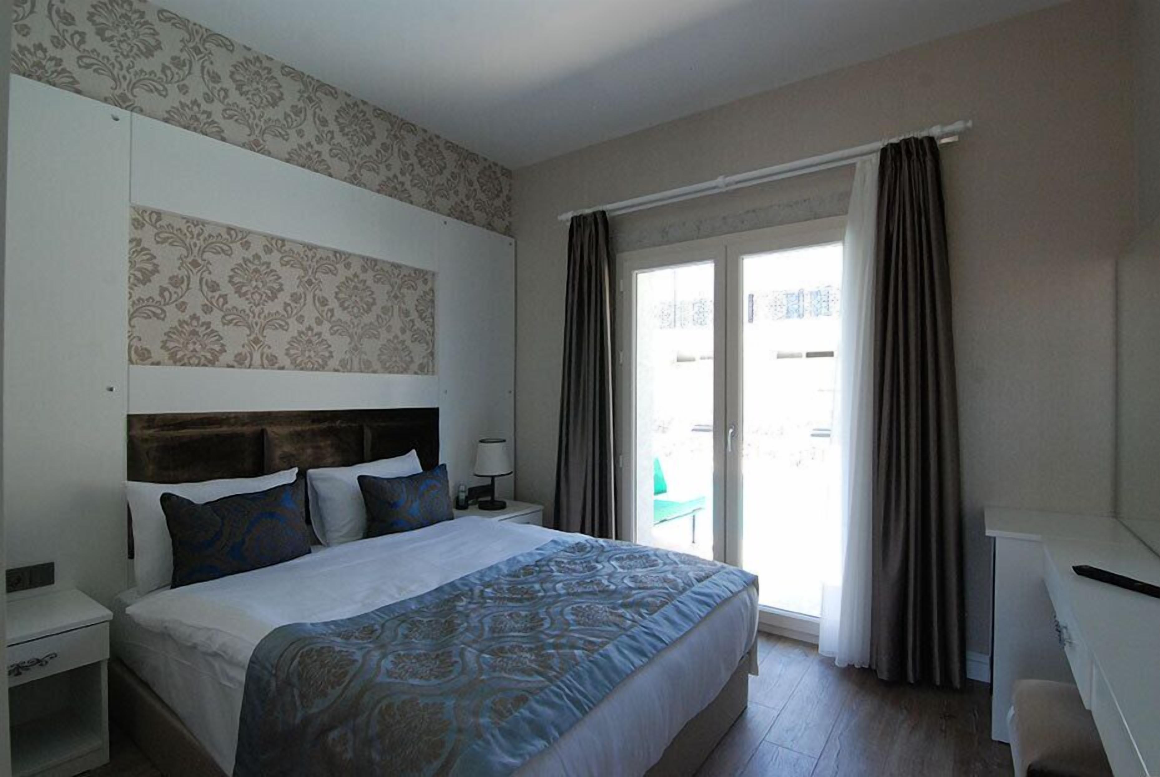 Une chambre d’hôtel avec un grand lit, une table de chevet, un bureau et une vue sur l’extérieur grâce à une porte-fenêtre coulissante.