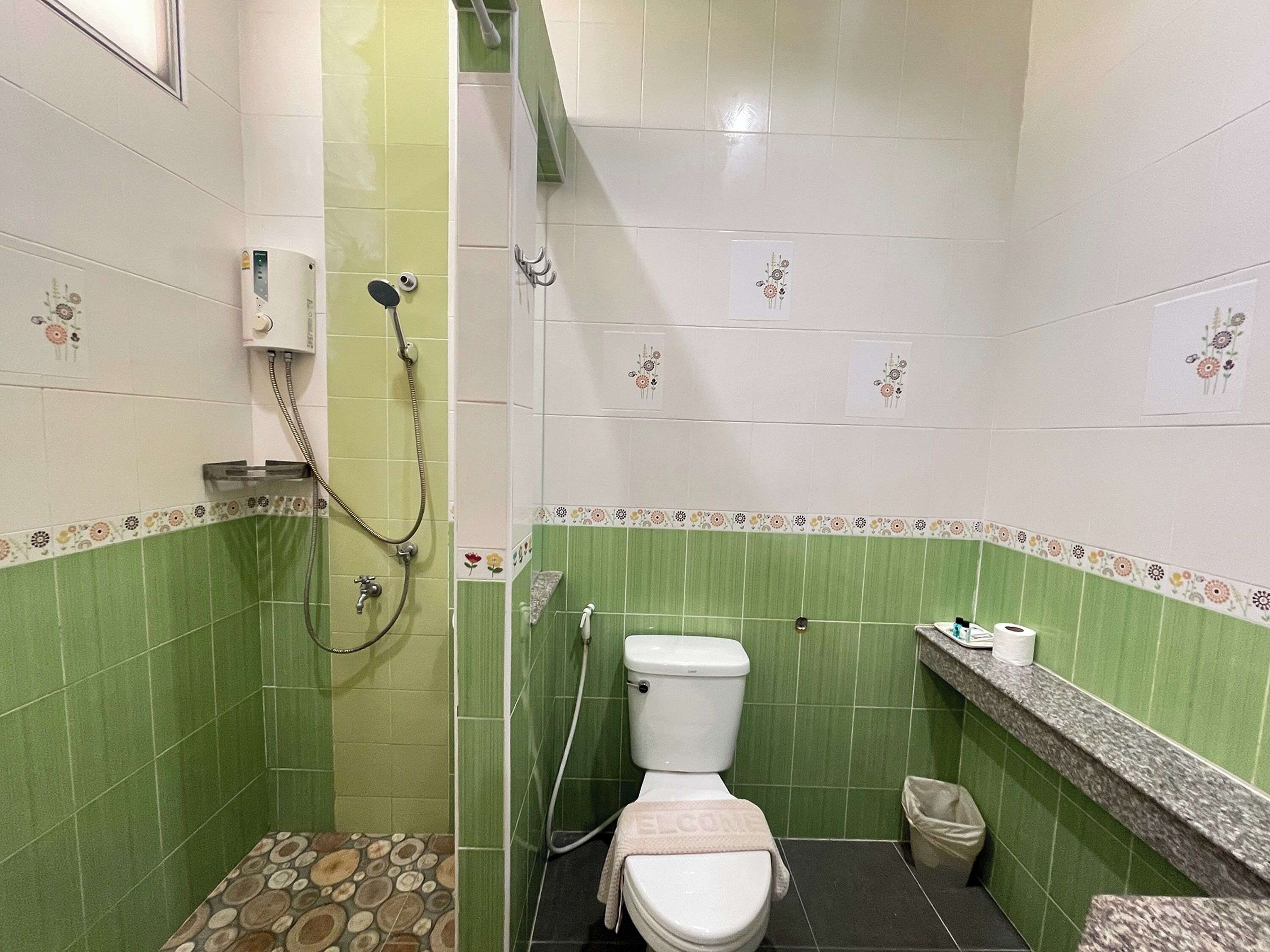 A bathroom with green tiles, a toilet, a shower, and a sink with a marble countertop.
