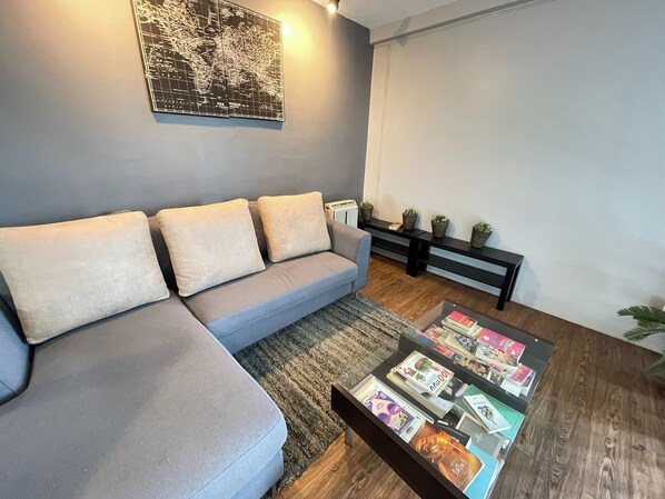 A modern living room with a grey sectional sofa, a coffee table with magazines, a world map on the wall, and a black console table with plants.