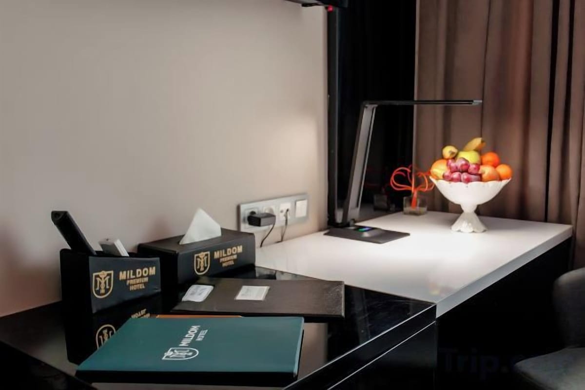 A hotel room with a desk, a bowl of fruit, a tissue box, and a power outlet.