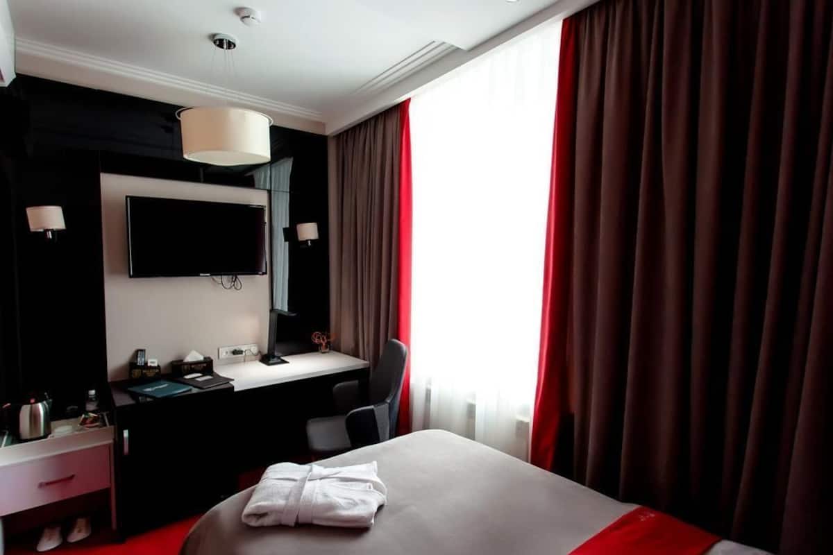 A hotel room with a bed, a desk, a chair, a television, and a window with curtains.