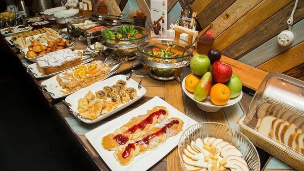 Mesa de buffet com diversos alimentos e uma cesta de frutas.