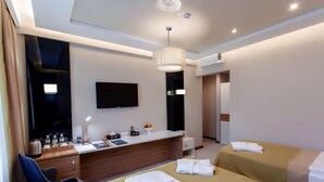 Quarto de hotel moderno com televisão de tela plana, escrivaninha com artigos de higiene pessoal, duas camas com toalhas e luminária de teto.