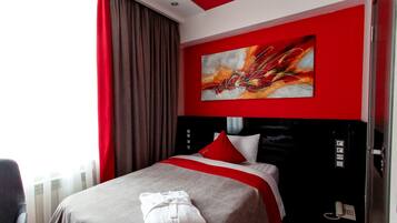Une chambre d’hôtel avec un lit, une literie rouge et blanche, un grand tableau abstrait et un rideau rouge.
