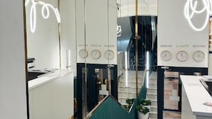Um hall de hotel moderno, com um balcão de recepção, uma escadaria e um espelho grande que reflete o interior.