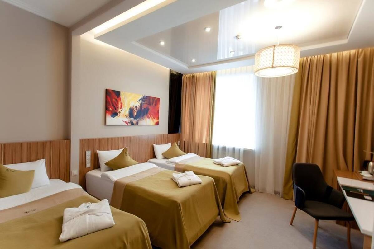 A hotel room with three beds, a desk, a chair, and a large window with curtains.