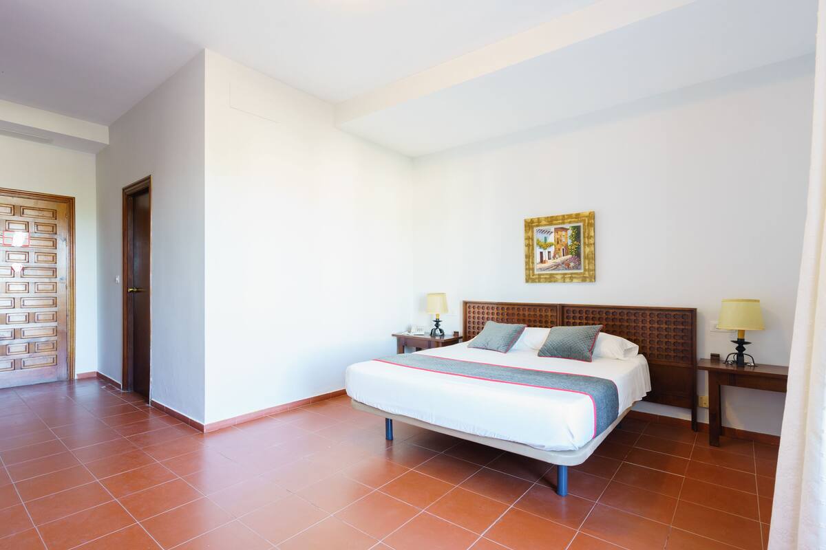 A hotel room with a bed, two bedside tables, a wooden headboard, a wall-mounted picture, and a door with a patterned design.