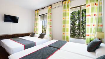 Habitación de hotel con dos camas, un televisor de pantalla plana montado en la pared y una ventana con cortinas.
