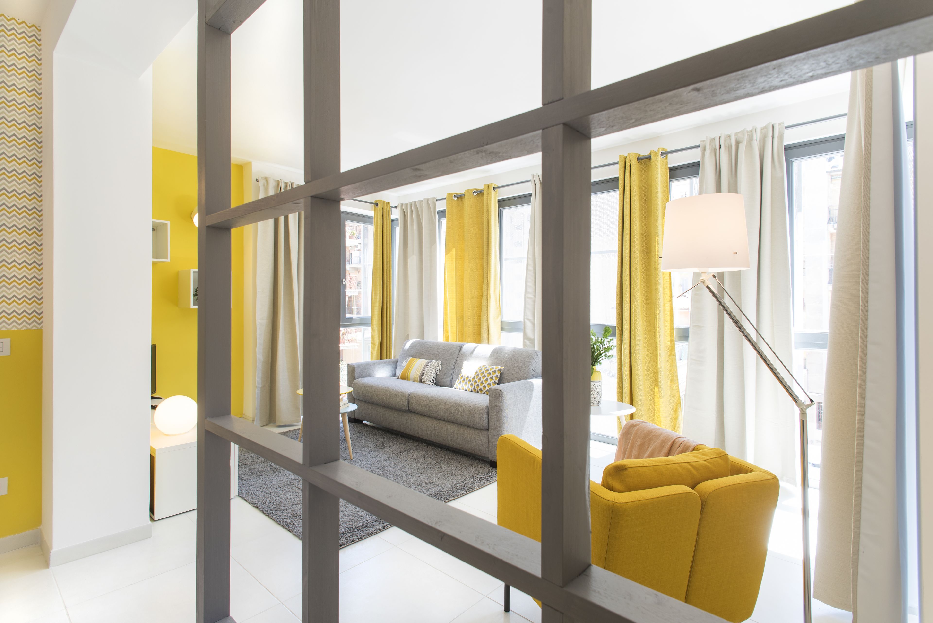 A modern living room with a sofa, yellow armchair, and a floor lamp.