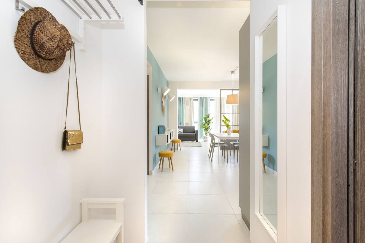 Un pasillo que conduce a un comedor con un banco, un sombrero y un bolso en la pared.