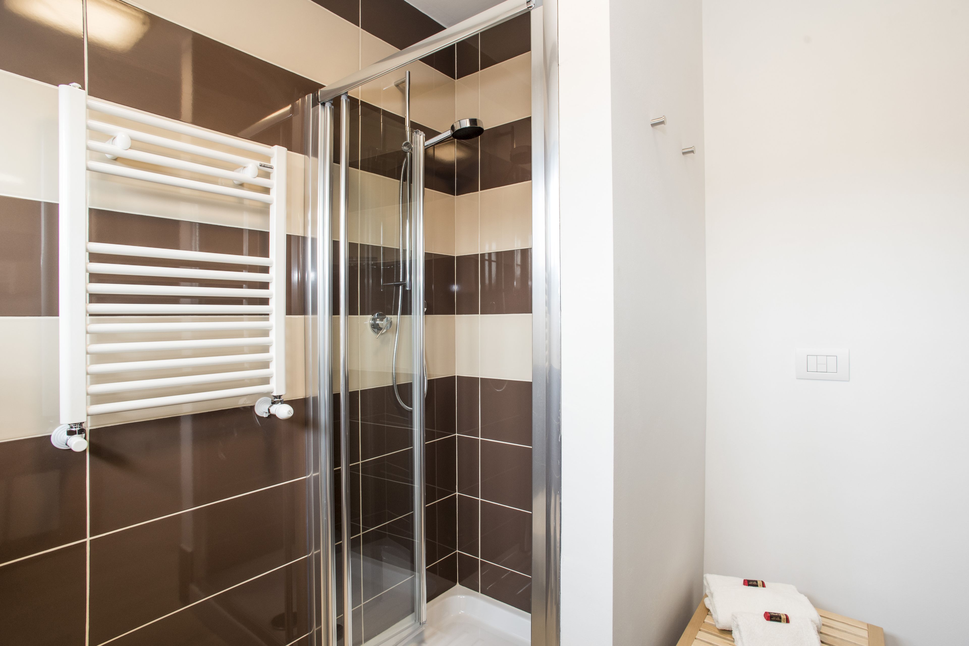 A modern bathroom with a glass-enclosed shower, a white towel rack, and a corner sink.