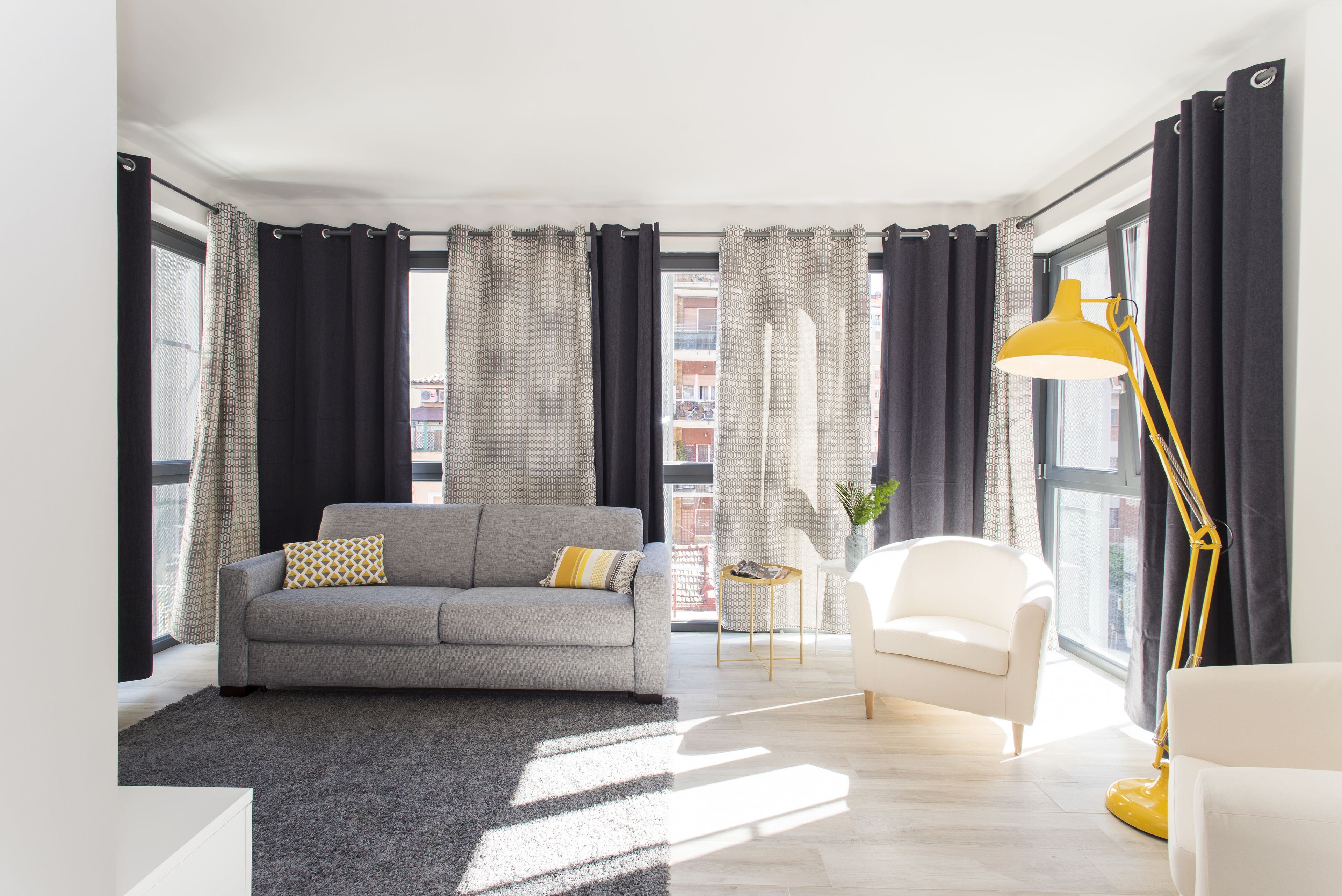 Een moderne woonkamer met een grijze bank, een witte fauteuil en een gele vloerlamp.